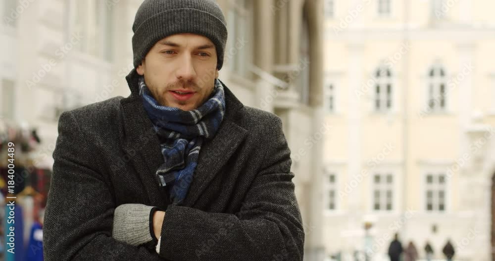 Portrait shot of the caucasian good looking man in casual style is freezing on the cold winter day while standing in the center city. Outside Portrait shot of the caucasian good looking man in casual style is freezing on the cold winter day while standing in the center city. Outside