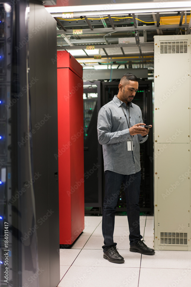 Server room technician looks down at his cellphone Server room technician looks down at his cellphone