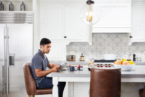 Man reading the newspaper in the morning at breakfast before work in kitchen