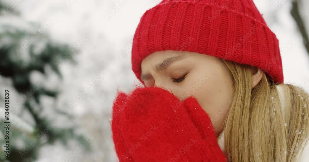 Close up of the attractive young blonde woman in red hat and gloves snoring on the street on cold frosty day and trying to get warm. Portrait. Outdoors Close up of the attractive young blonde woman in red hat and gloves snoring on the street on cold frosty day and trying to get warm. Portrait. Outdoors