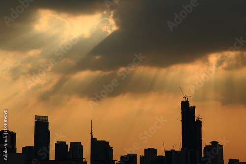 silhouette cityscape with powerful sun light beaming through dark cloudy sky.