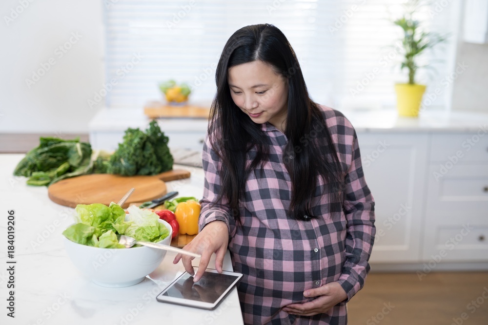 Pregnant woman using digital tablet in kitchen Pregnant woman using digital tablet in kitchen