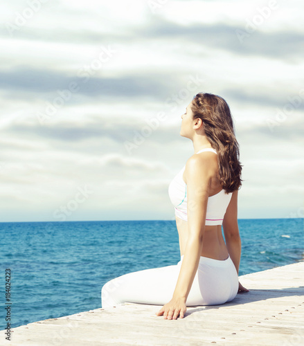 Attractive woman in white sporty clothes doing yoga on a wooden pier. Yoga, sport, leisure, recreation and freedom concept. © Acronym