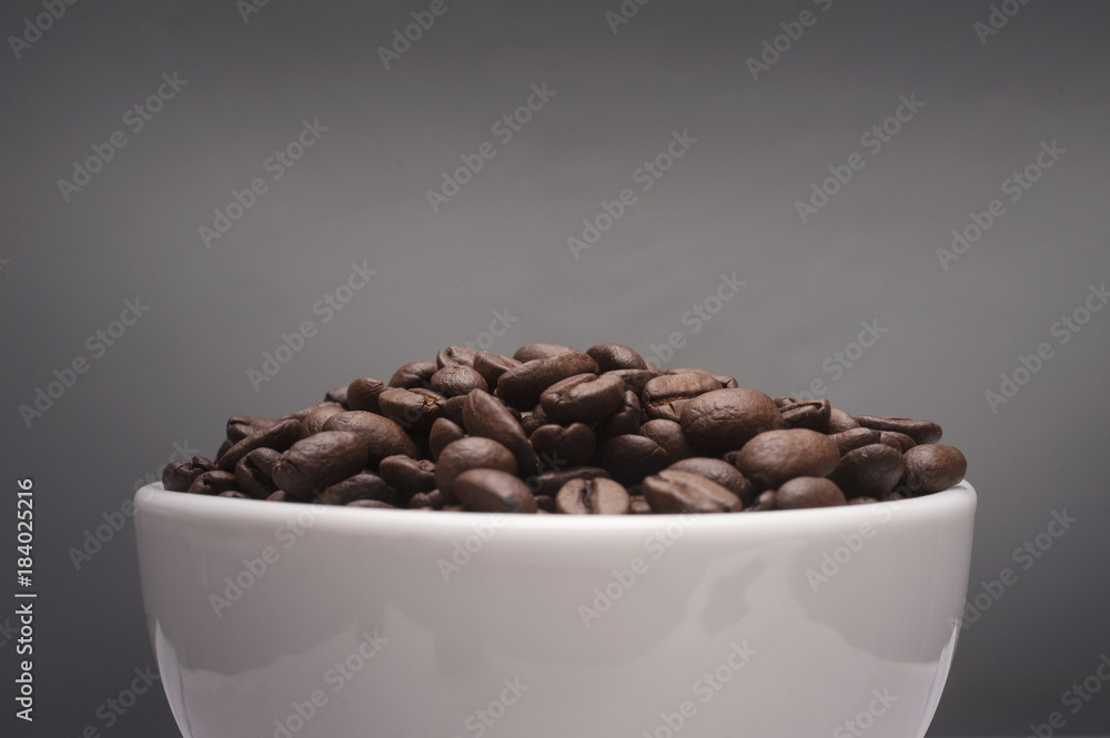 Coffee beans in a white cup with grey background.Close up shot with selective focus. Coffee beans in a white cup with grey background.Close up shot with selective focus.