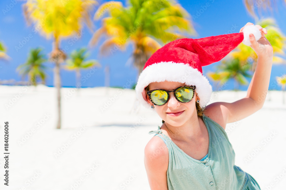 Obraz premium Happy funny little girl in Santa hat during Christmas beach vacation have a lot of fun
