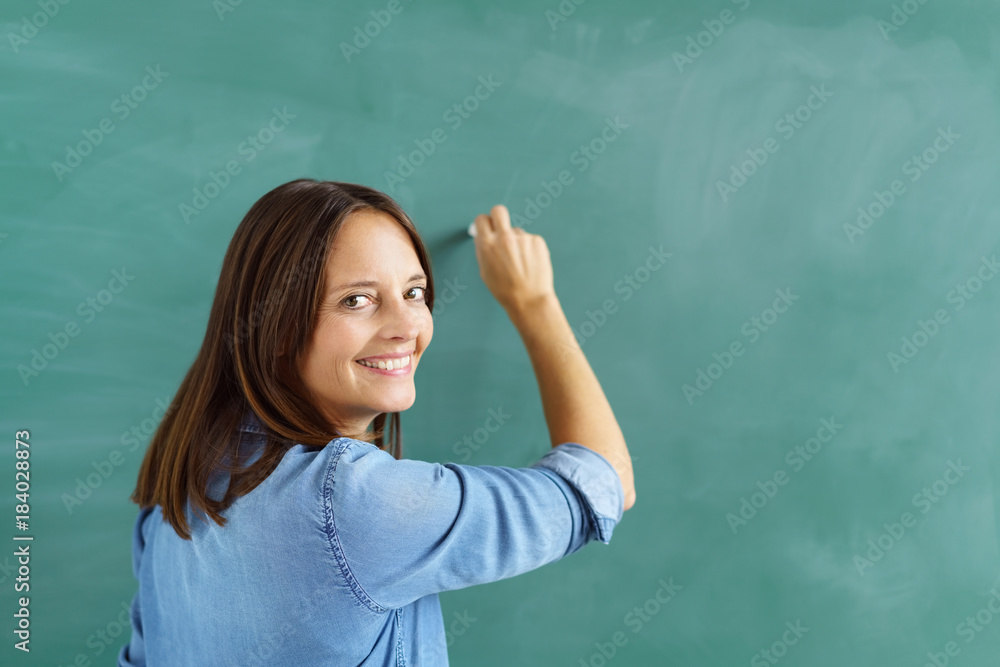 lehrerin schreibt an die tafel und schaut über die schulter zurück lehrerin schreibt an die tafel und schaut über die schulter zurück