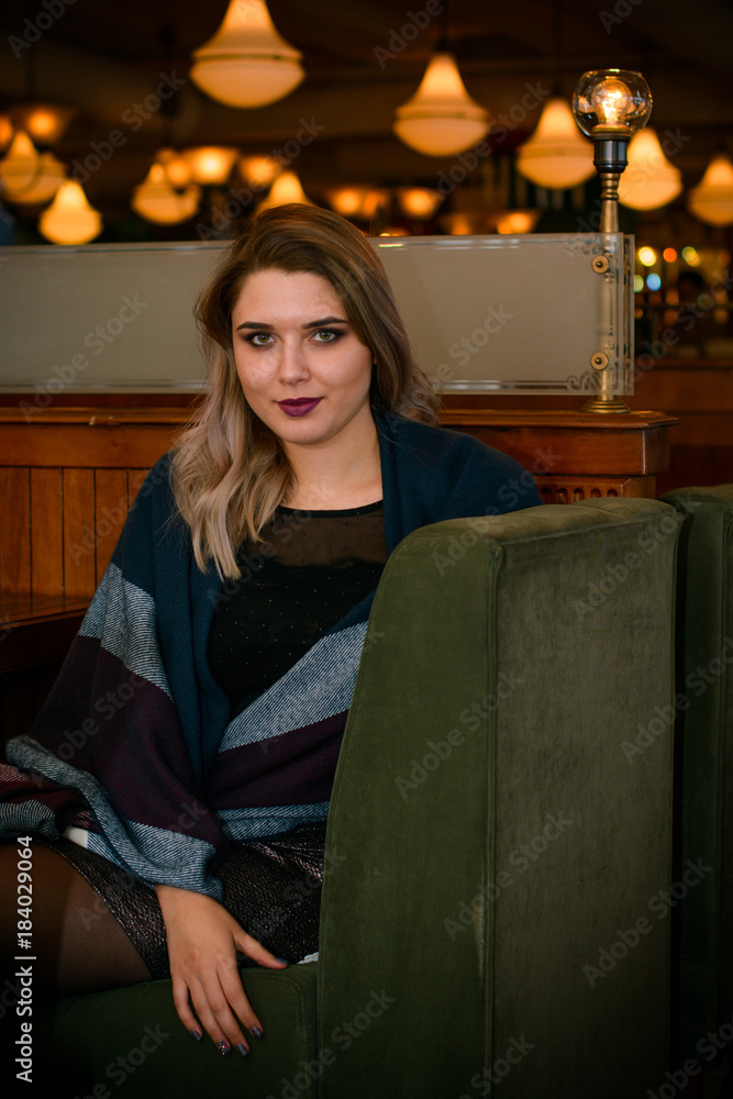 Young elegant plus size woman in cozy atmosphere restaurant. Lady wait on a date in romantic mood. Portrait in deep vintage tones Young elegant plus size woman in cozy atmosphere restaurant. Lady wait on a date in romantic mood. Portrait in deep vintage tones