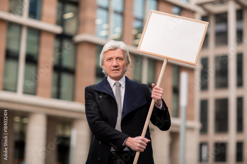 Grey-haired businessman showing protest banner while expressing his attitude photo