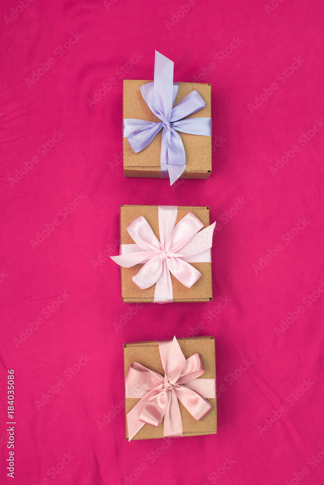 Three gift boxes tied with satin coloured ribbon on a pink background a Red heart. Three gift boxes tied with satin coloured ribbon on a pink background a Red heart.