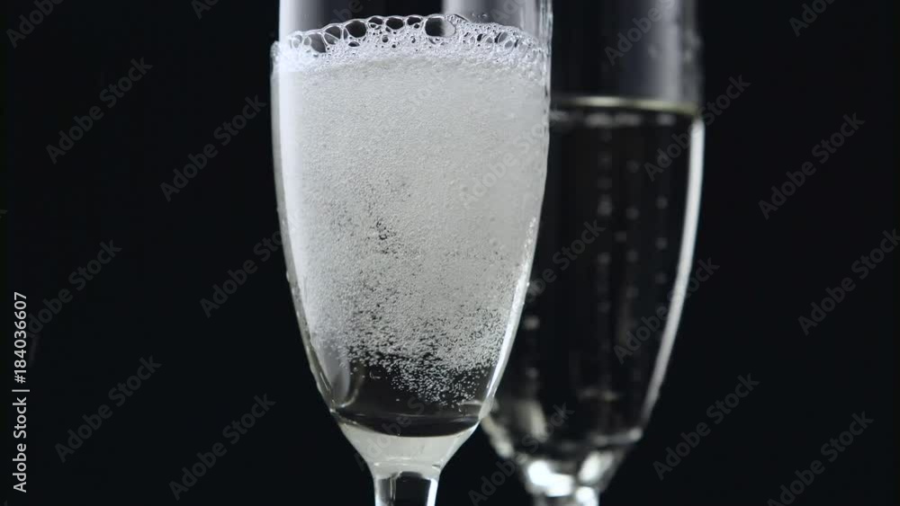 Champagne pouring from bottle into two glasses on black background. Close up Champagne pouring from bottle into two glasses on black background. Close up