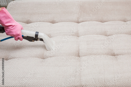 Dry cleaner's employee hand cleaning a sofa with professionally extraction method. Textile upholstered furniture. Early spring regular cleanup. Commercial cleaning company concept.