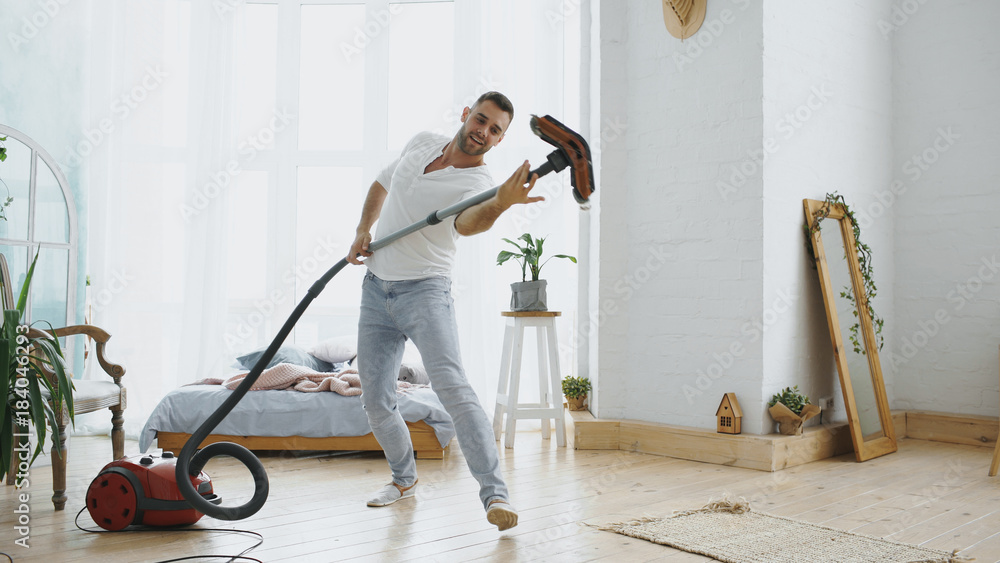 Young man having fun cleaning house with vacuum cleaner dancing