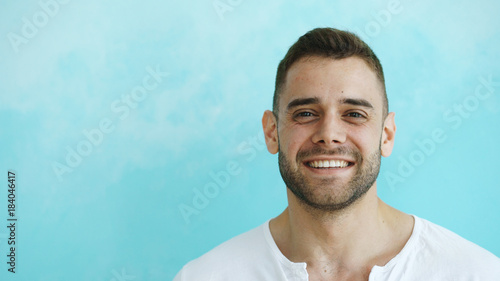 Closeup portrait of young smiling and laughing man looking into camera on blue background