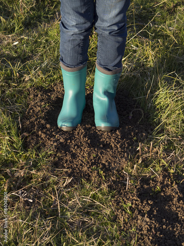 Woman's feet with blue rubber boots standing on grass