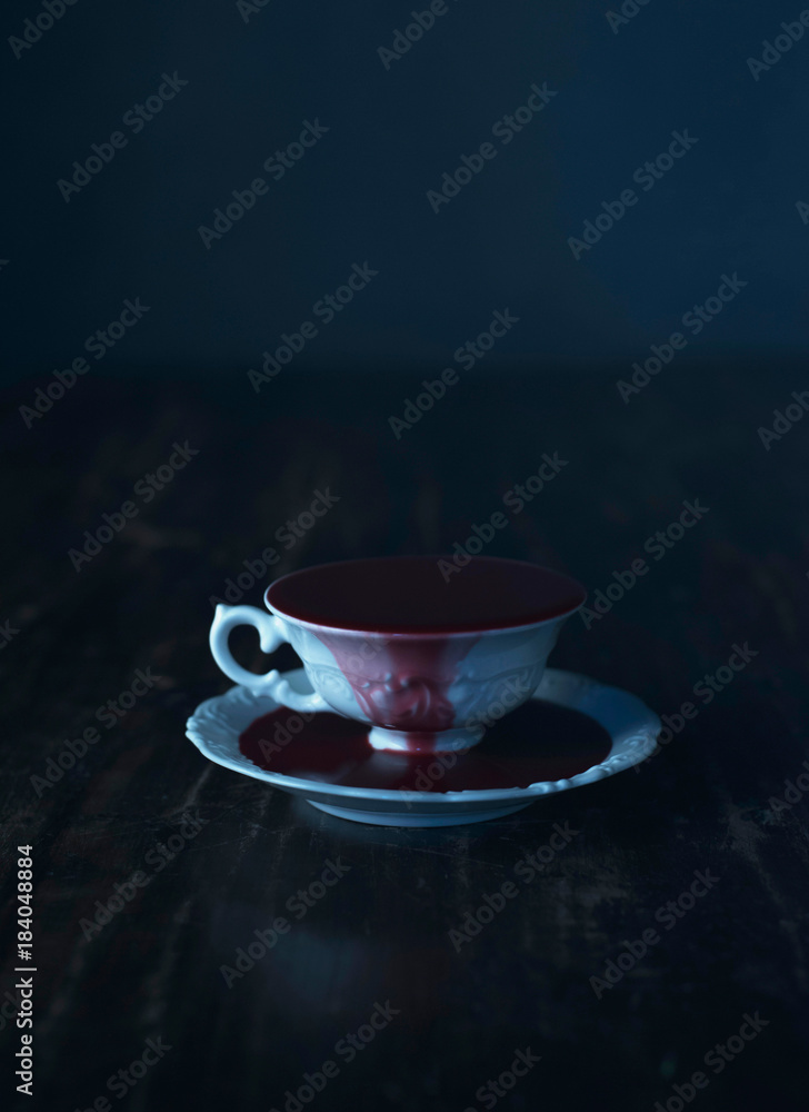 Fototapeta premium White tea cup in dark blood on wooden table.