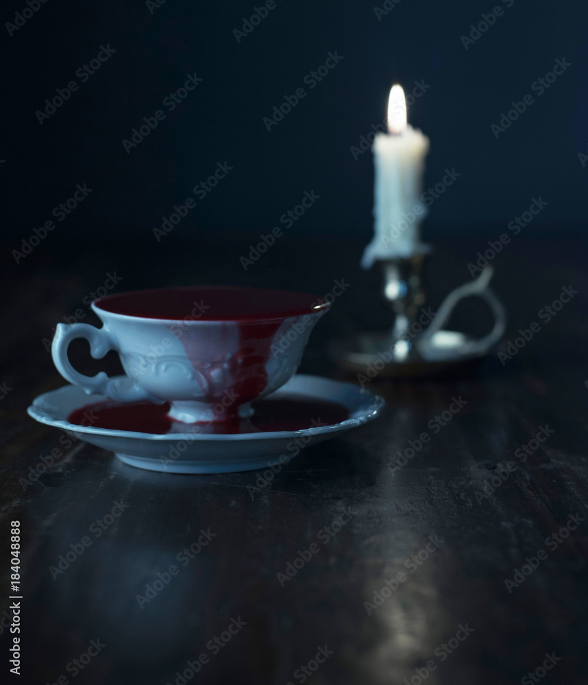 Fototapeta premium White tea cup in dark blood on dark wooden table with burning candle in candleholder.