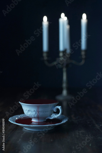 White tea cup in dark blood on dark wooden table with burning candles in candleholder. photo