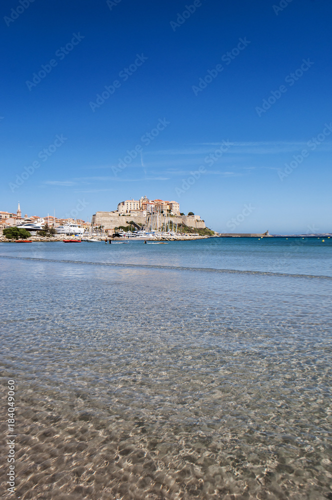 Corsica, 03/09/2017: il Mar Mediterraneo e la spiaggia con vista sullo skyline dell'antica Cittadella di Calvi, con le sue antiche mura e le barche nel porto turistico