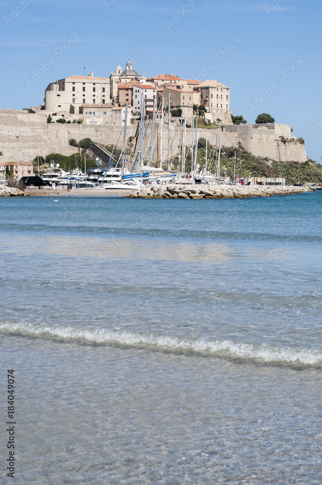 Corsica, 03/09/2017: il Mar Mediterraneo e la spiaggia con vista sullo skyline dell'antica Cittadella di Calvi, con le sue antiche mura e le barche nel porto turistico