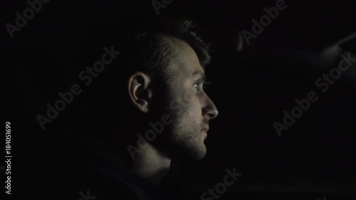 Man drives a car on the highway in the night and is lit by headlights