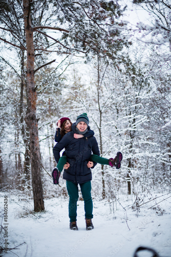 Young beautiful couple having fun in the snow covered forest park. New Year and winter clothes concept
