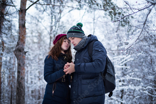Young lovely couple warming up each others hands in snowy winter forest park. New Year, Christmas and winter clothes sale concept