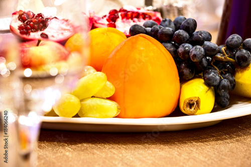 Still life. Fruit in a plate on the table. Pomegranates  apples   bananas  grapes and persimmons