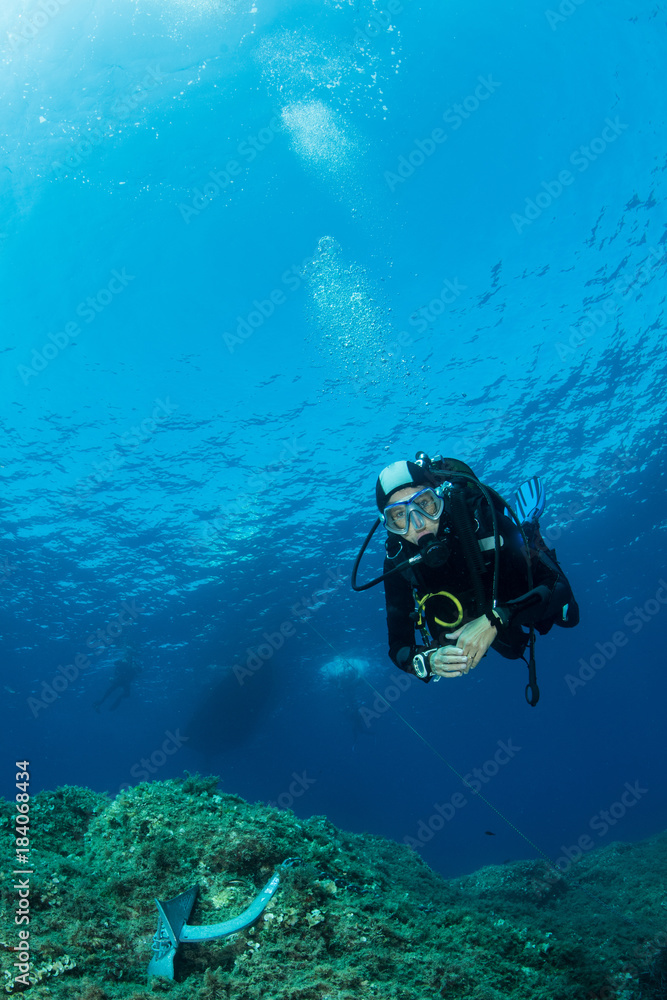 woman scuba diving over rocks in the Mediterranean Sea woman scuba diving over rocks in the Mediterranean Sea