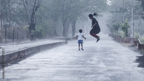 Tableau sur toile Mother and daughter welcoming the first monsoon showers by playing in heavy rain