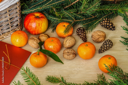 A full basket of ripe fruits. Mandarins, oranges, apples, lemons, walnuts against the backdrop of branches from a Christmas tree.