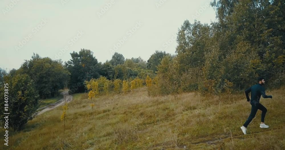 Runner going fast uphill on a cross country path. Drone side view. Concentrated athlete sportsman achieving life goal. Runner going fast uphill on a cross country path. Drone side view. Concentrated athlete sportsman achieving life goal.