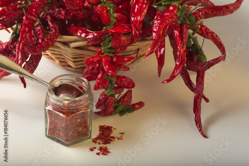 Peperoncino rosso piccante macinato nel vasetto di vetro, con peperoncini sani essiccati nel cesto.  photo