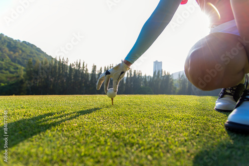 Lady golfer places a golf ball and tee in the ground evening time. Lifestyle Concept.