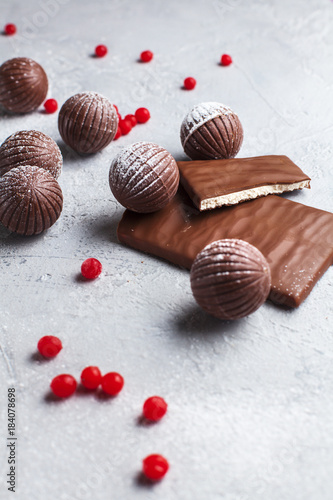 chocolate round candies, chocolate bars and red berries on a gray background and powdered sugar