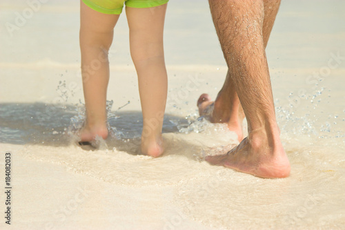 Dad and son are walking along the beach. Close-up of legs.
