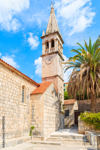 Church building and palm tree against sunny blue sky in Splitska village on Brac island, Croatia