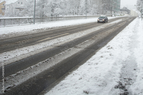 Car driving along the mud street while it is snowing in the winter