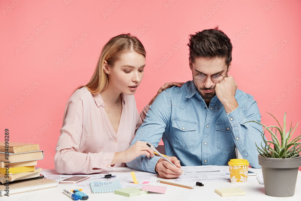 Affectionale lovely female tries to help her husband, looks attentively what man writes, wants to give some advice how make financial report correctly and encourage him. People and team work concept