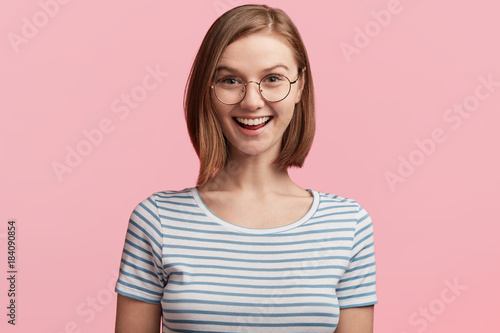 Excited positive attractive woman glad to recieve present she dreamt about all life, can`t believe eyes, being thankful to relatives who prepared surprise, wears casual clothes and round glasses
