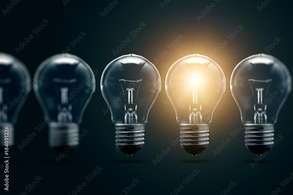 A series of electric light bulbs, only one glows, against a dark background. The concept of several attempts, one successful. A successful idea. A series of electric light bulbs, only one glows, against a dark background. The concept of several attempts, one successful. A successful idea.