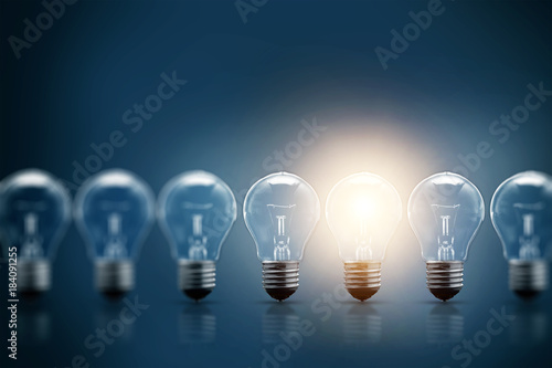 A series of electric light bulbs, only one glows, against a dark background. The concept of several attempts, one successful. A successful idea.