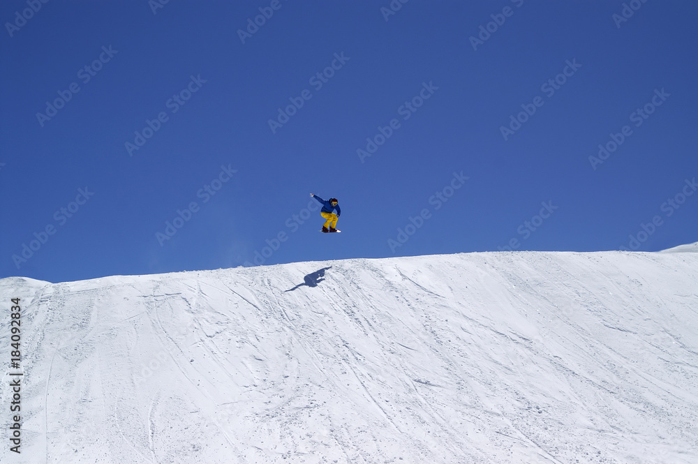 Snowboarder jumping in terrain park on sun winter day