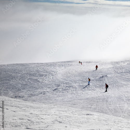 Skiers and snowboarders downhill on snowy slope and sunlight sky in haze