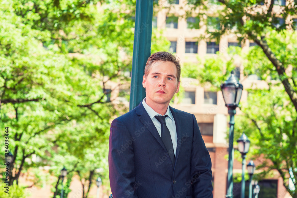 Portrait of Businessman. Dressing in dark blue suit, black tie, a young guy standing against light pole on street in New York, looking up, thinking. Concept of business and environment protection... Portrait of Businessman. Dressing in dark blue suit, black tie, a young guy standing against light pole on street in New York, looking up, thinking. Concept of business and environment protection...