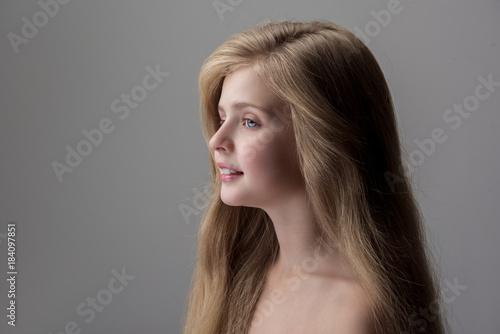 Enjoying day. Side view of joyful lovely little girl is standing with naked shoulders and looking forward with slight smile. Isolated background with copy space in the left side