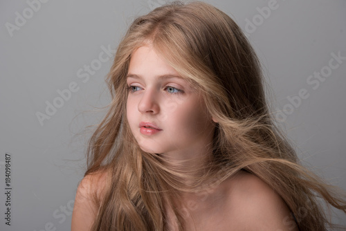 Sweet little girl with long hair is looking aside dreamily. Isolated background