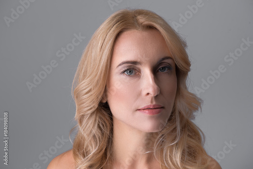 Close-up portrait of pensive middle-aged naked woman. She is looking at camera calmly. Isolated background