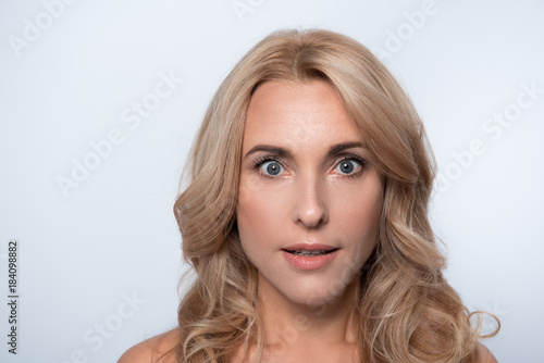 Wow. Portrait of lovely elegant amazed middle-aged woman with long hair. She is looking at camera in wide-eyed surprise. Isolated background