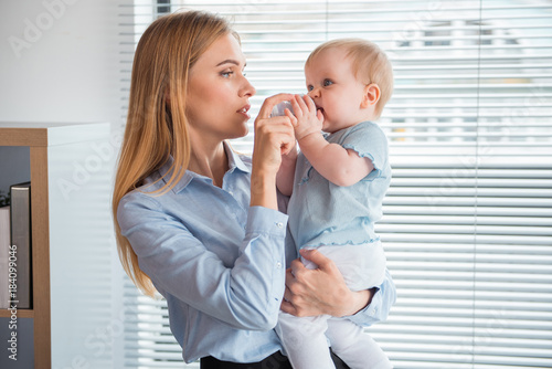 Photography Side view serene mother feeding calm baby from bottle while keeping it on hands in office
