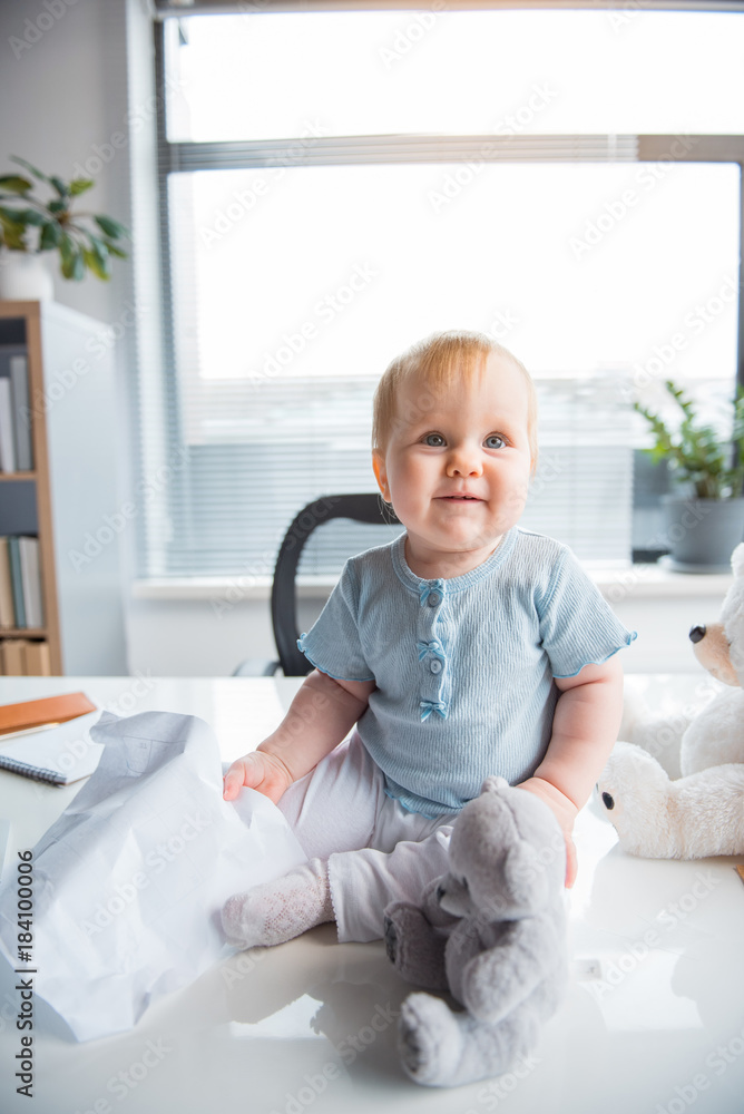 Portrait of smiling baby playing with toys while locating on desk in modern office. Kid at work concept